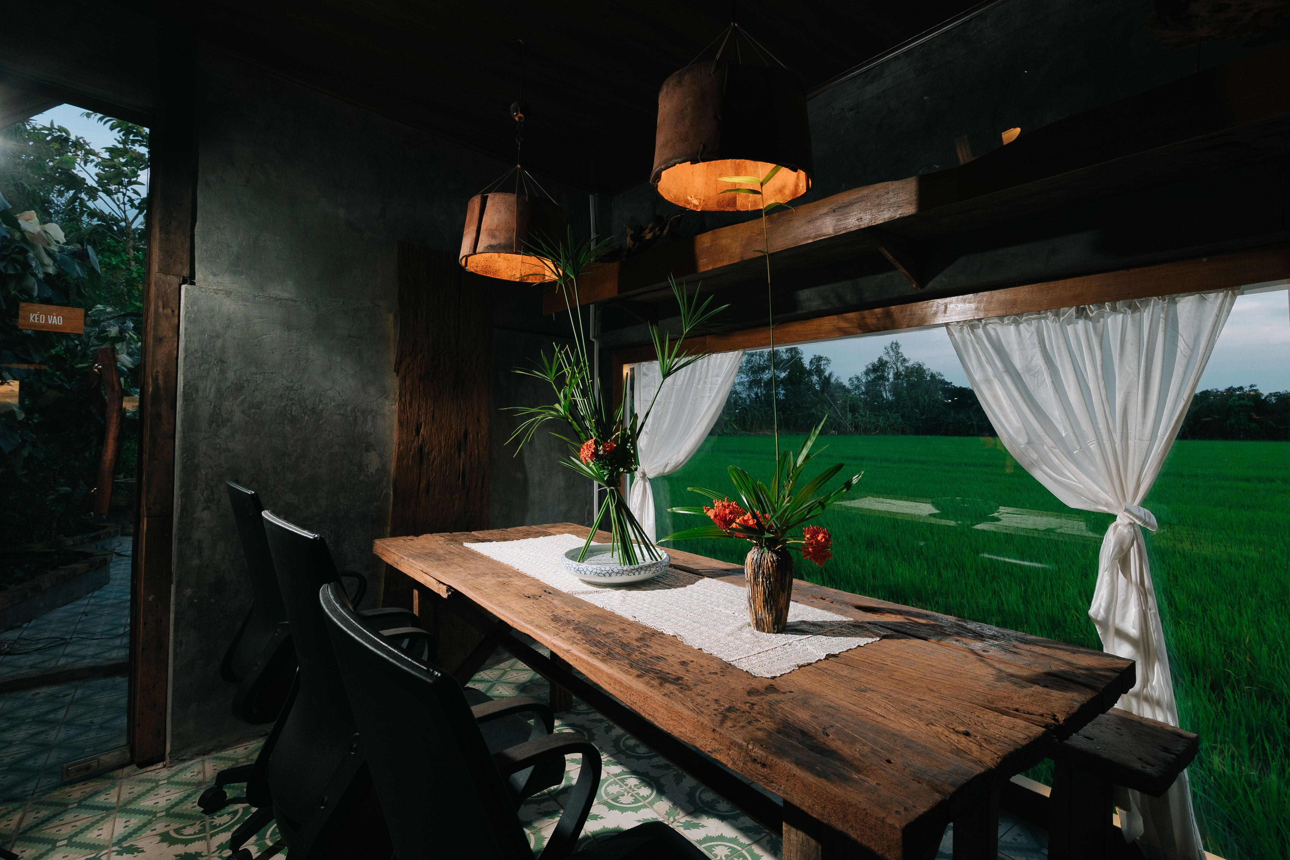 Rustic indoor dining space with a view of a green field, featuring natural wood and floral decor.