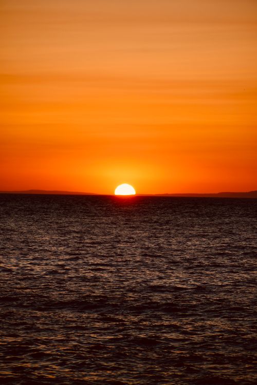 Free Captivating sunrise over the ocean with a bright orange sky reflecting on the water. Stock Photo