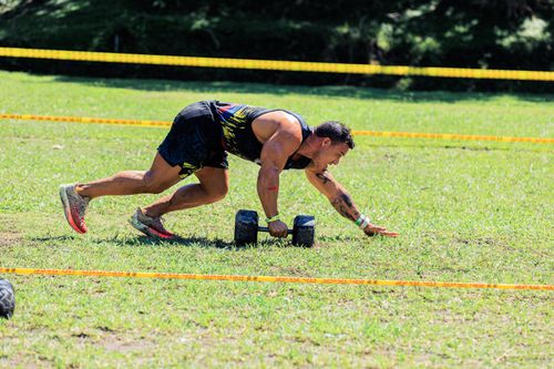 Free Athlete competing outdoors using dumbbells on a green field in a fitness competition. Stock Photo