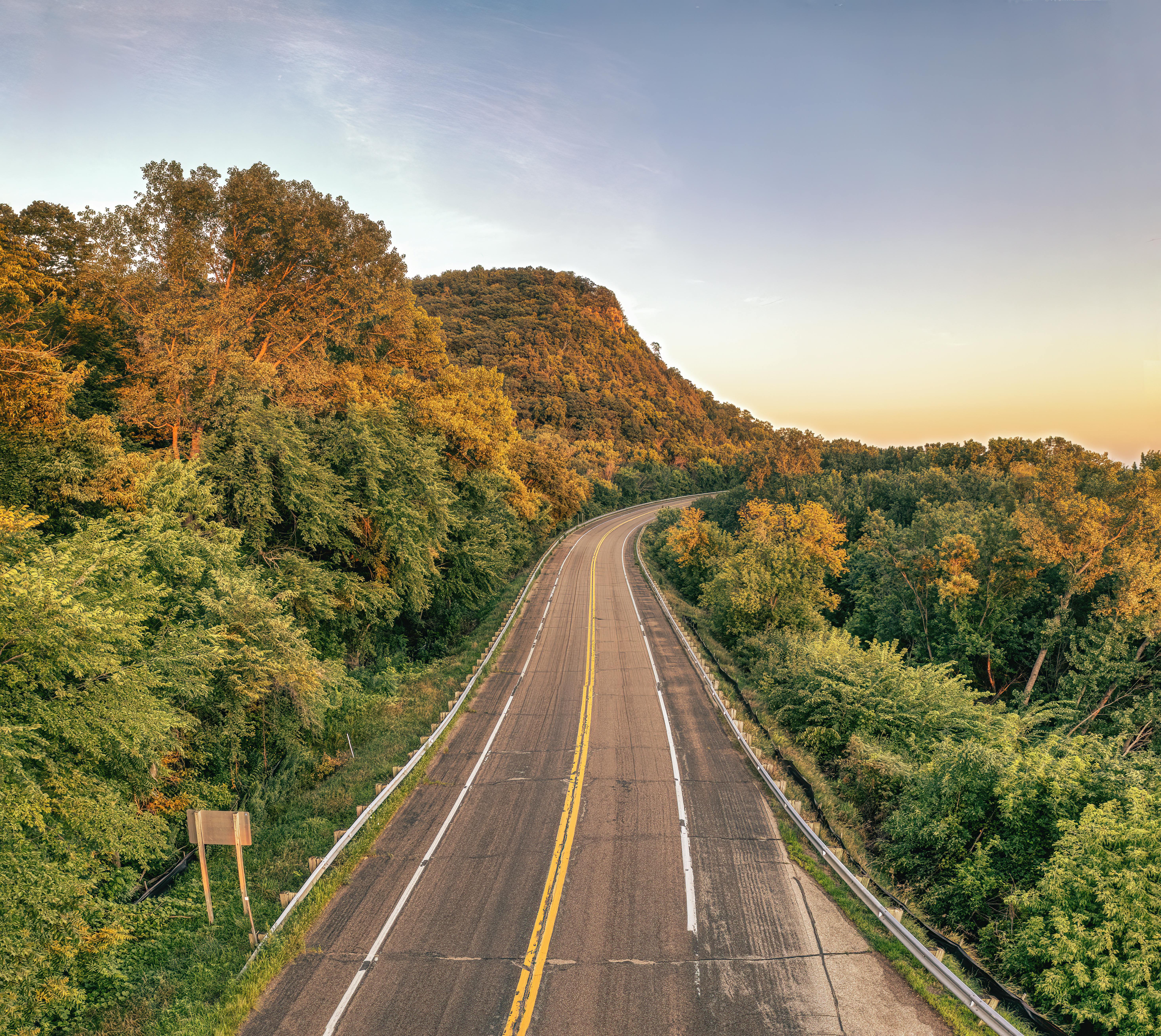 A winding road cuts through a verdant forest during a summer sunset in Stockholm, Wisconsin, USA.
