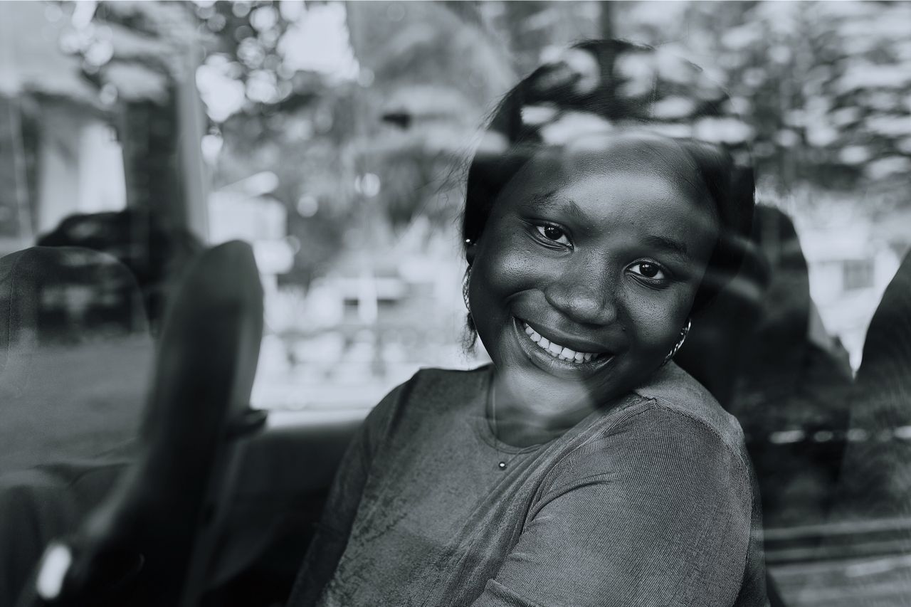 black and white portrait of a smiling woman seen through a car window