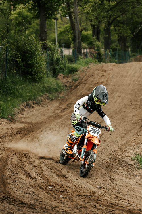 Free Youth motocross racer speeding on a dirt track with green surroundings. Stock Photo