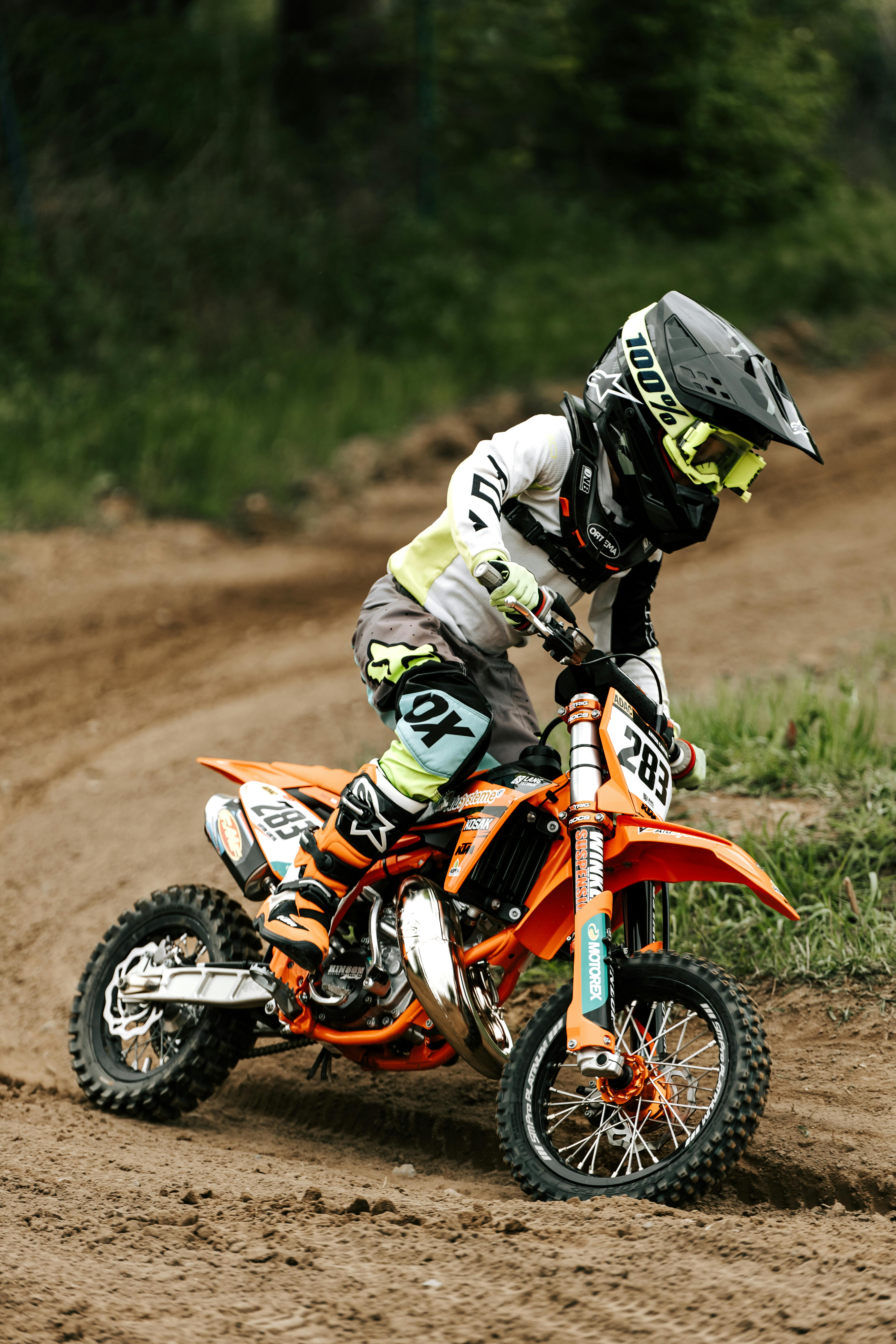 A young child riding a dirt bike on a muddy track, showcasing skills and focus in outdoor motocross sports.