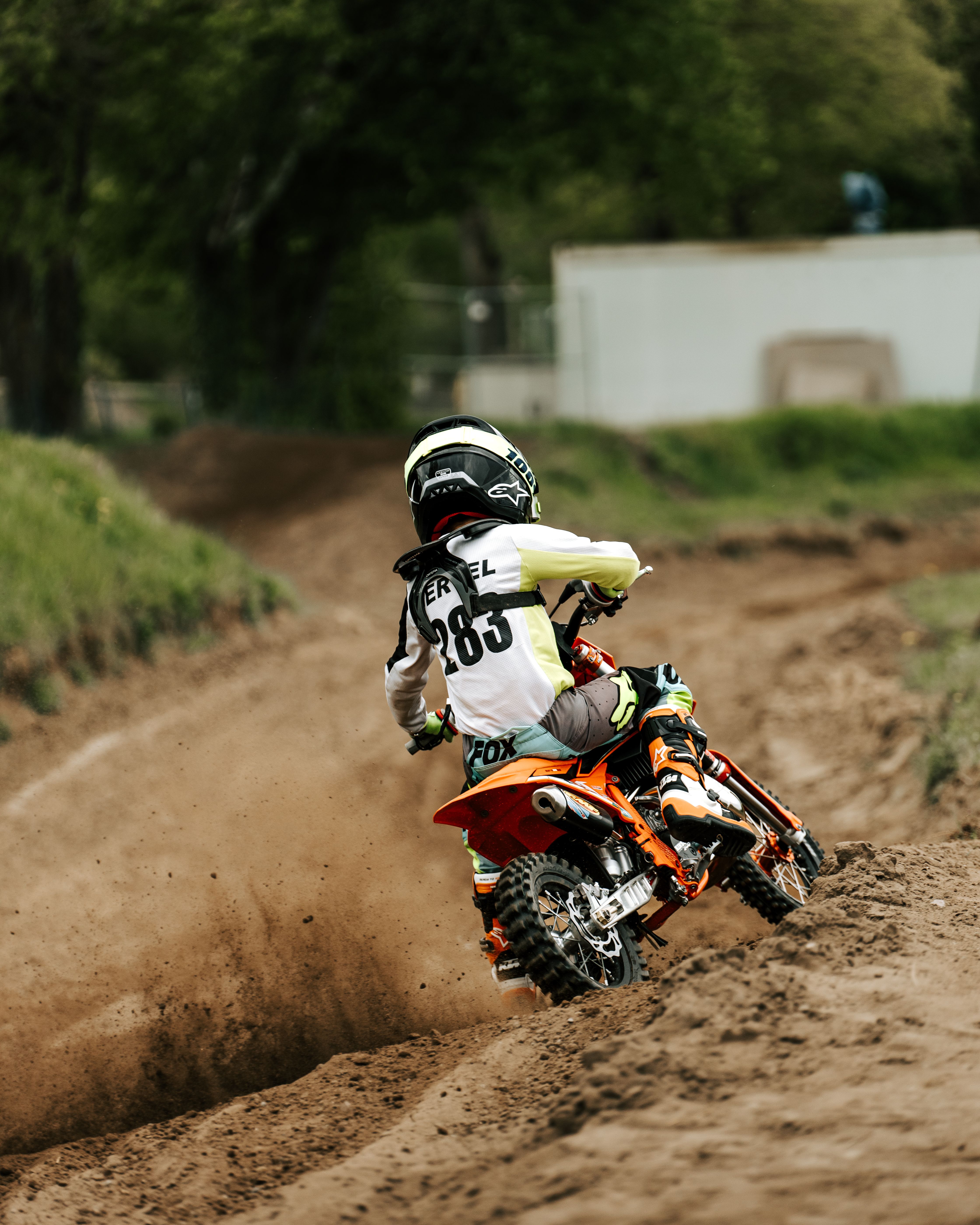 Young motocross racer skillfully navigating a dirt track during a sunny day.