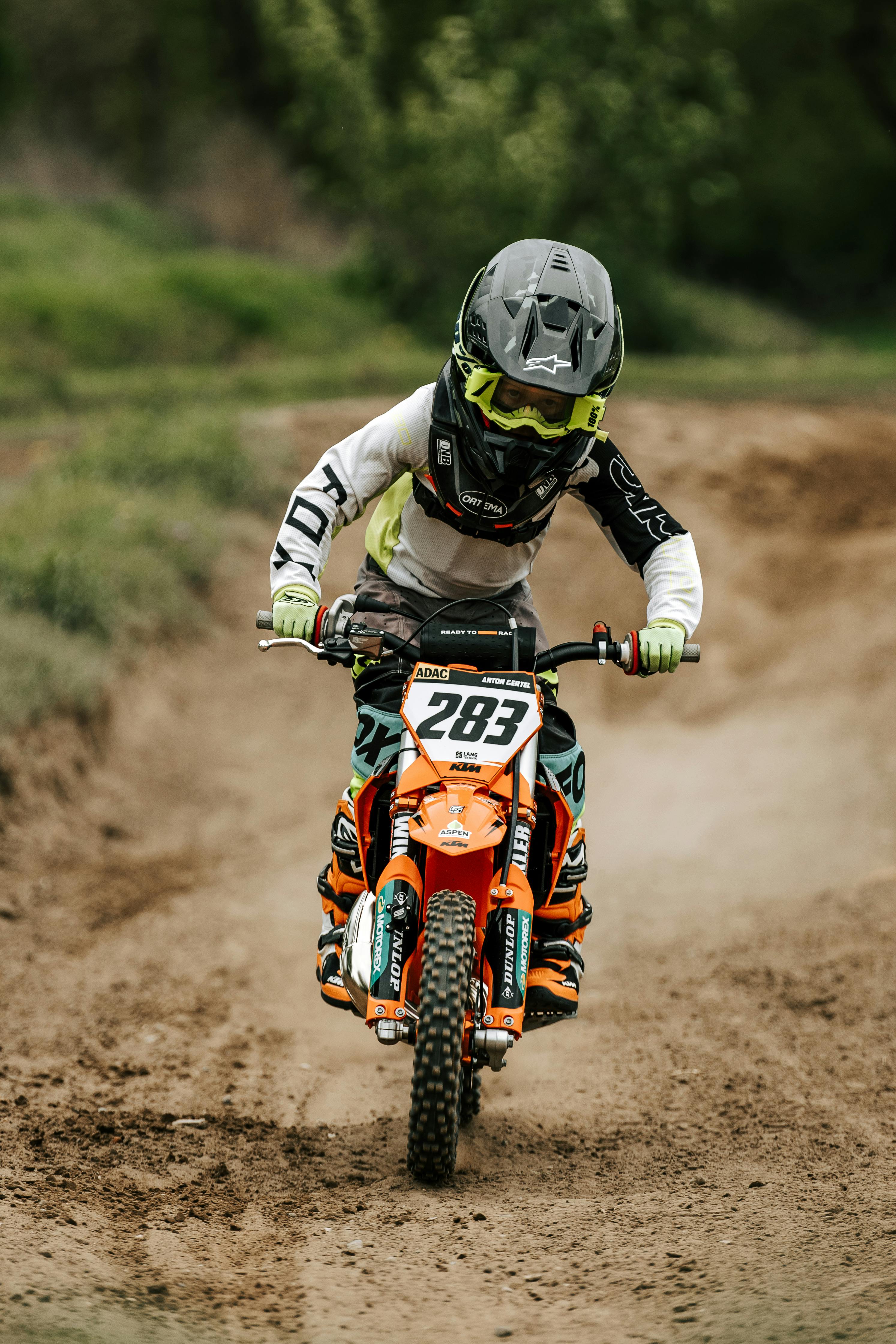 Young rider on dirt bike racing outdoors, showcasing motocross skills and gear.