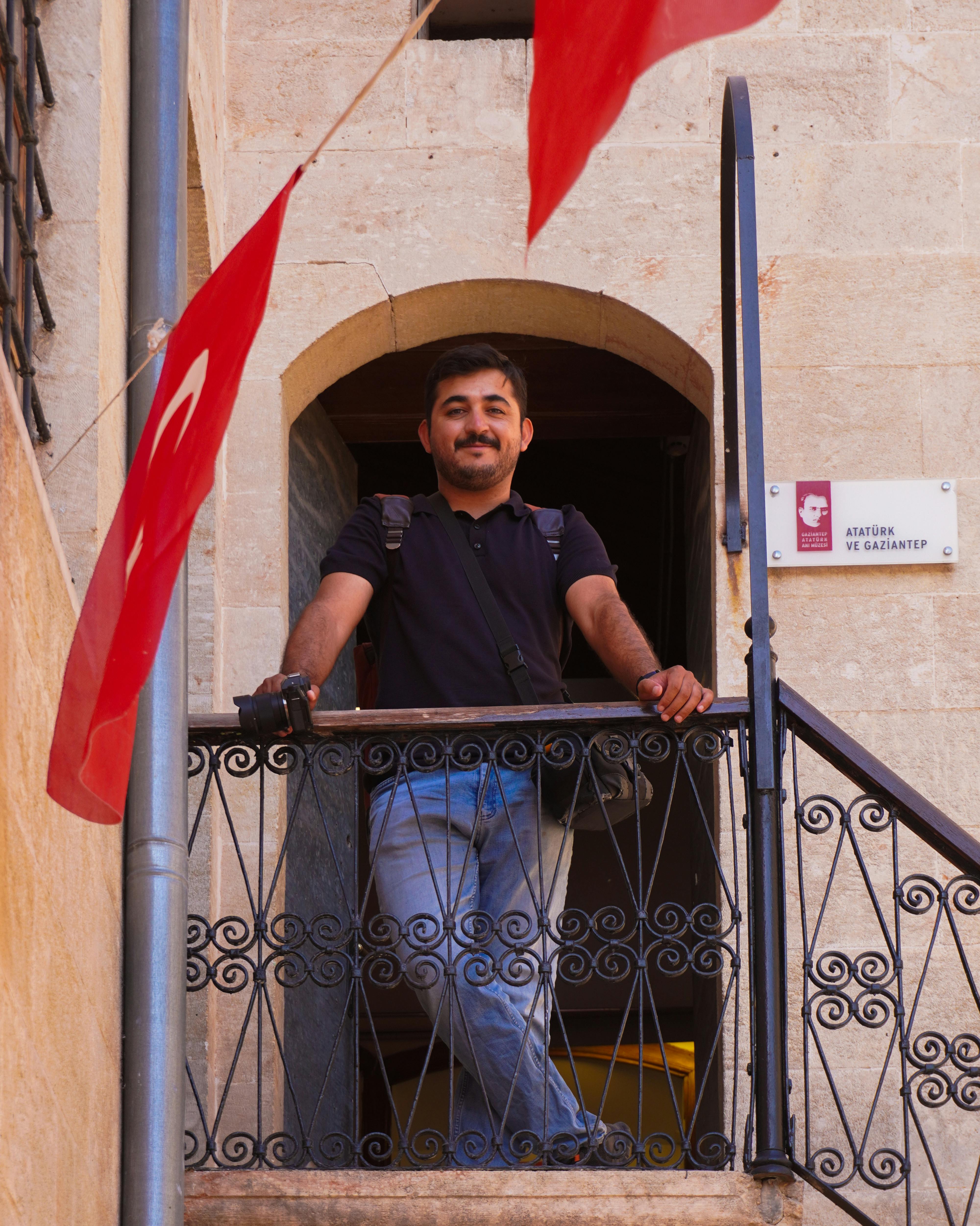 A man stands on a balcony in Gaziantep, Turkey, with Turkish flags in view.