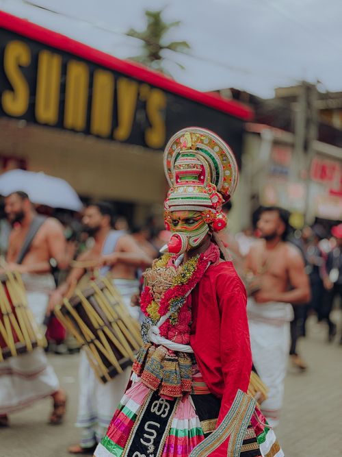Free Colorful Theyyam performer in traditional attire with drummers at Ernakulam festival, Kerala, India. Stock Photo