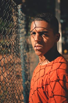 在城市环境中，一名年轻人靠在铁丝网栅栏上，投下戏剧性的阴影