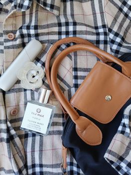 Stylish flat lay of perfume, bag, and plaid shirt, perfect for fashion and lifestyle imagery.