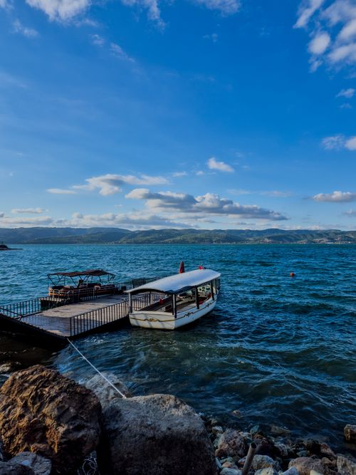 Free Idyllic view of a white boat docked on a tranquil lake under a vivid blue sky with clouds. Stock Photo