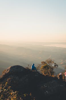 Hikers sit atop a mountain, enjoying a breathtaking sunrise over a vast landscape.