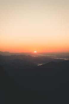 A stunning sunset over rolling hills and mountains, casting a golden hue.