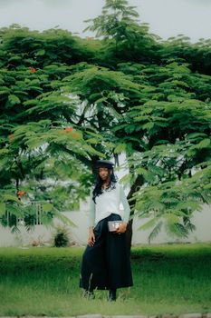 Elegant woman standing under vibrant trees in Abuja, Nigeria, capturing peaceful nature vibes.