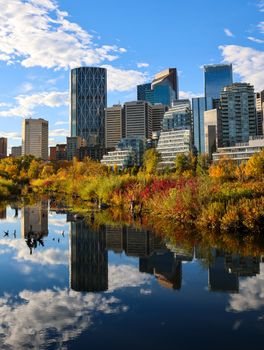 Stunning view of Calgary's skyline reflected in a river surrounded by vibrant autumn foliage.