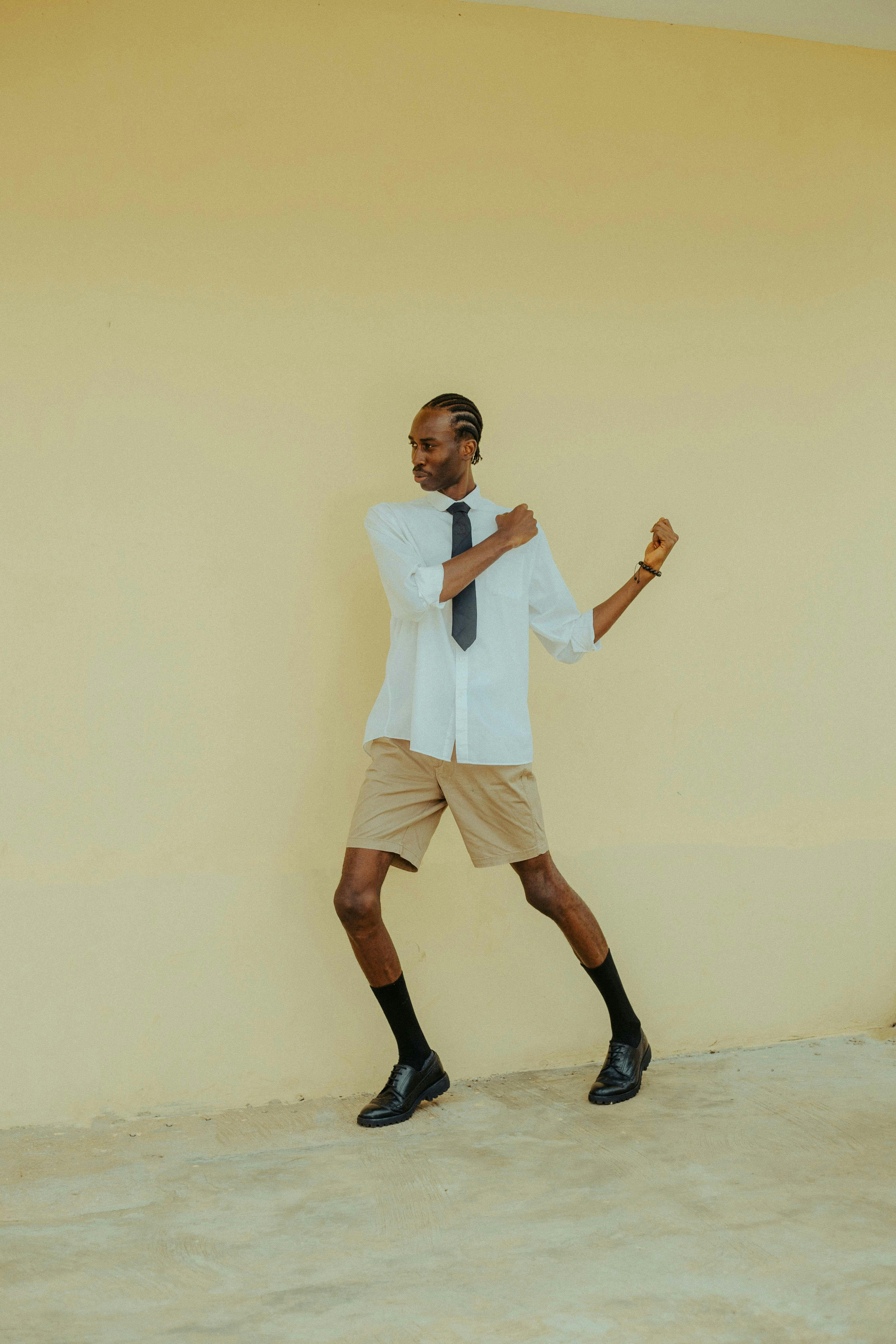 Stylish man with braids poses confidently against a neutral backdrop in Ibadan, Nigeria.