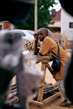 Young person in a market setting selling sugarcane, wearing casual attire, outdoors.