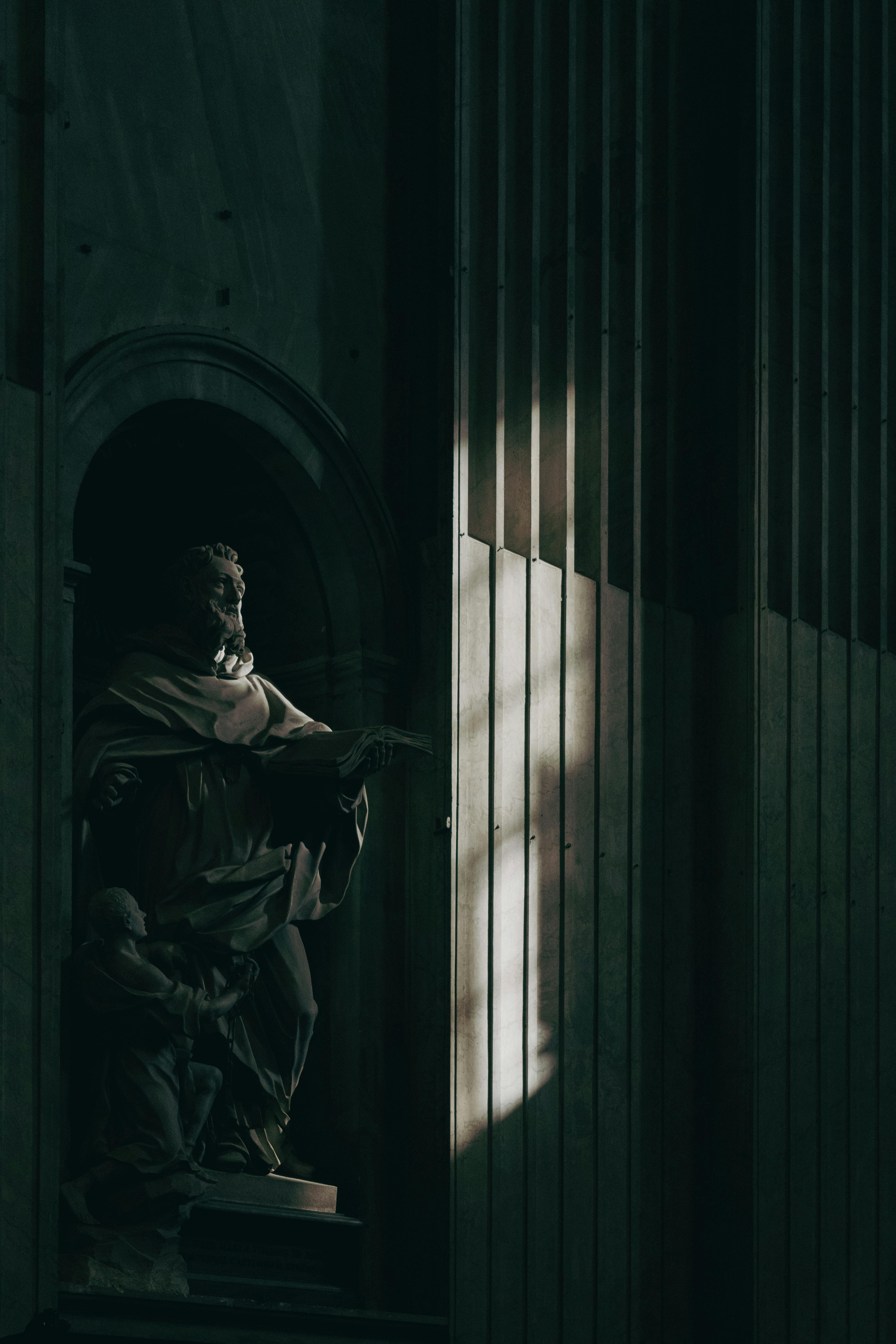 Intricate Roman statue engulfed in shadow and light in a historic Lazio building.