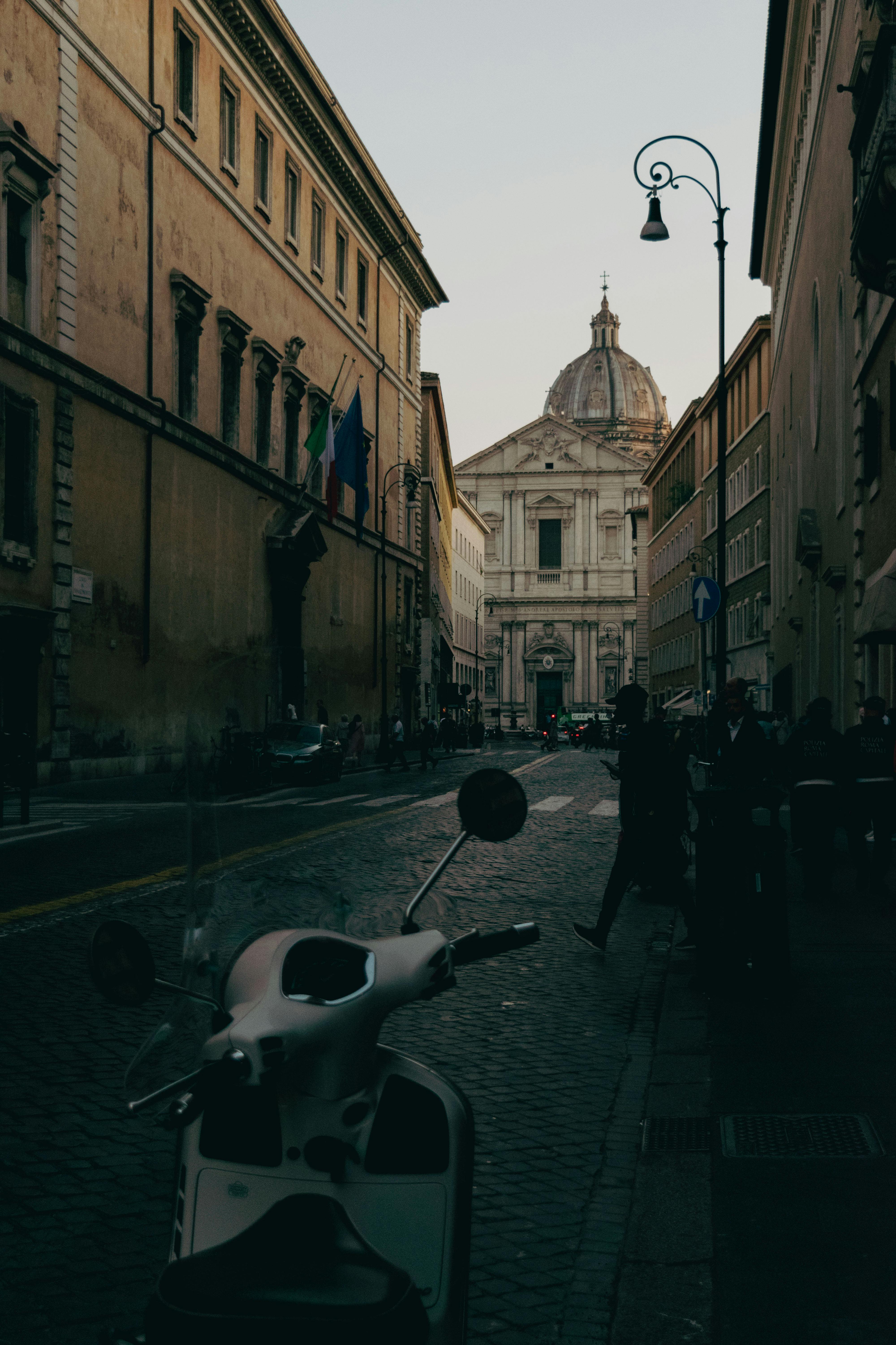 Capture the essence of Rome with this street view featuring iconic architecture and a scooter.