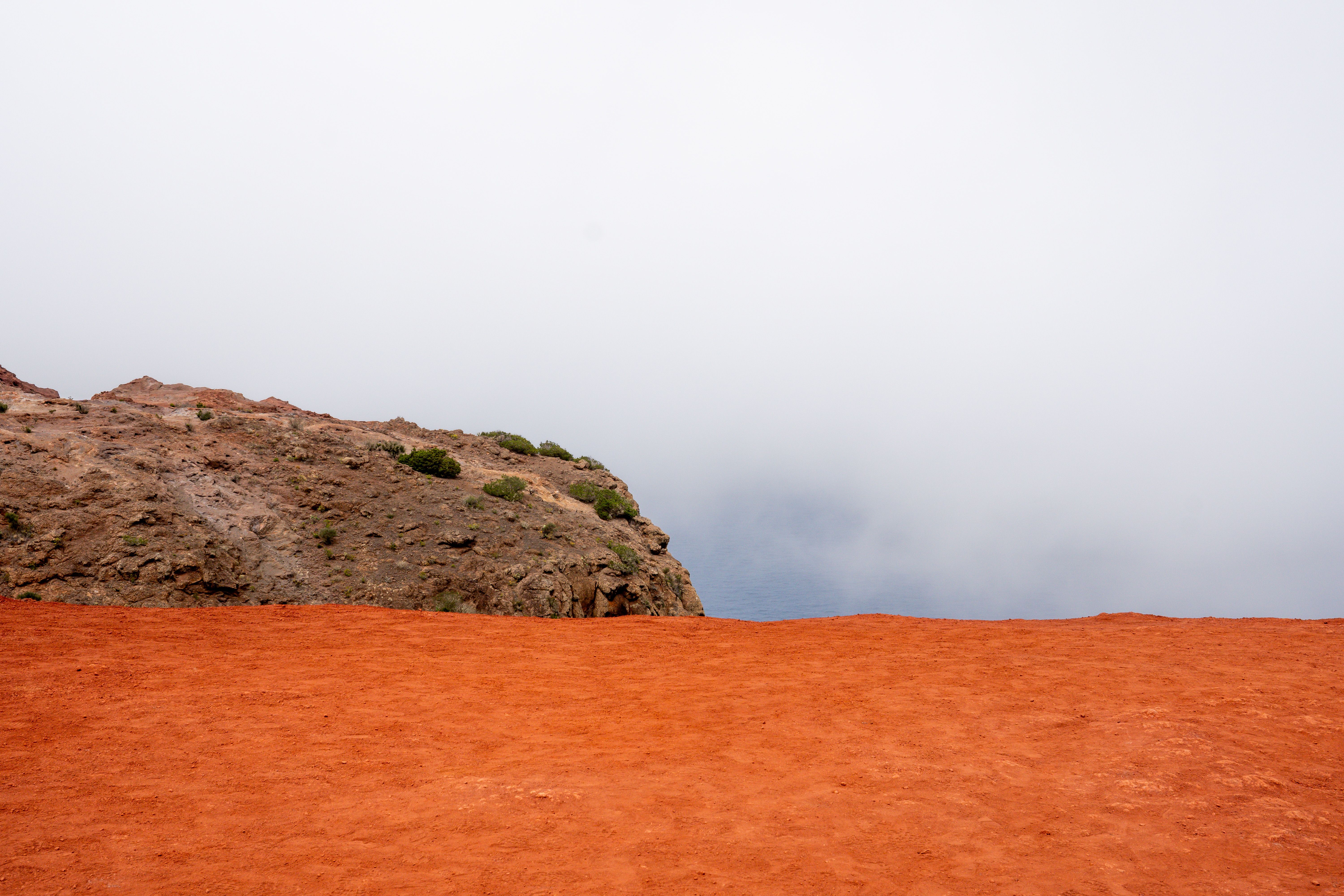 Breathtaking view of red earth meeting the cliffs under a misty sky in Agulo, Canary Islands.