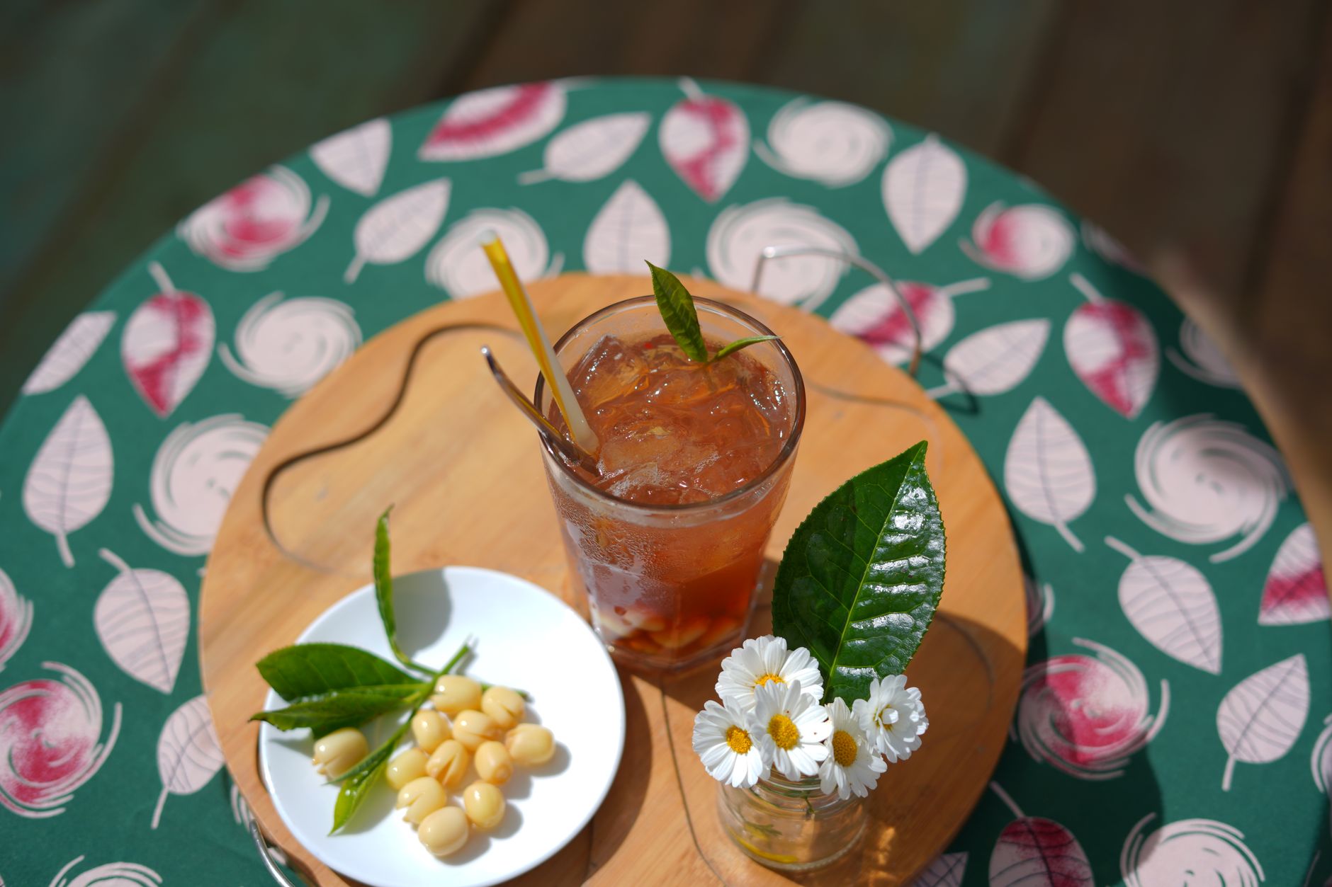 A vibrant iced tea with lotus seeds, garnished with daisies, shot outdoors in Dalat, Vietnam.