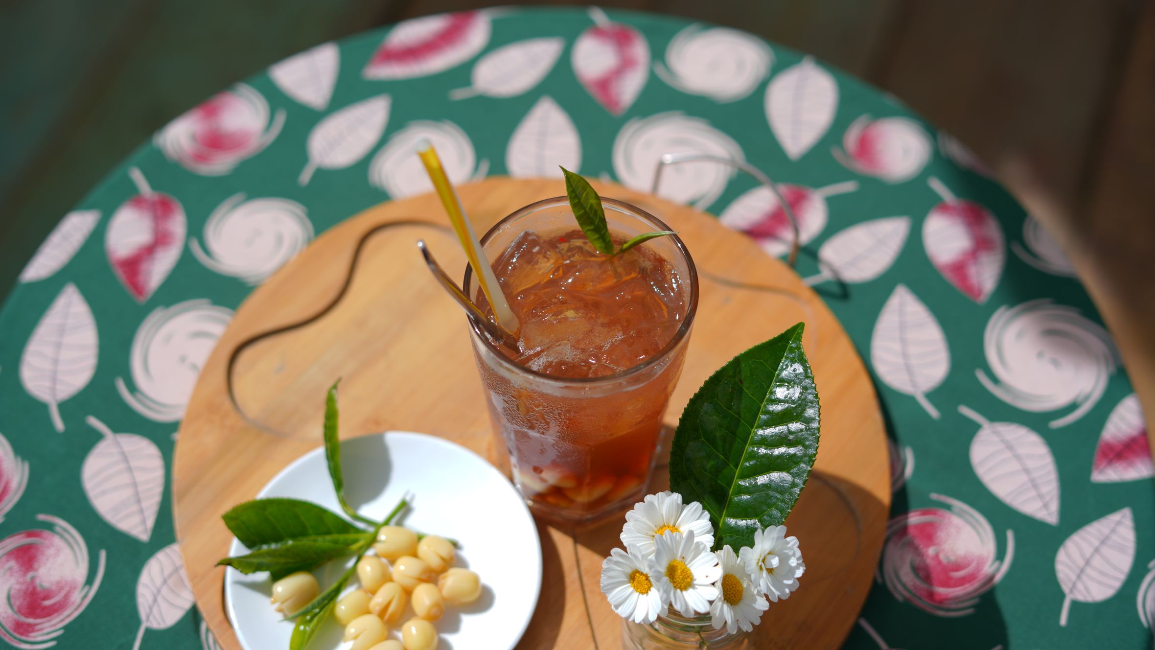 A vibrant iced tea with lotus seeds, garnished with daisies, shot outdoors in Dalat, Vietnam.
