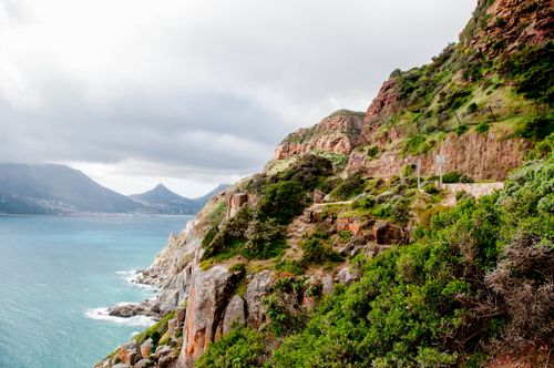 Free Picturesque view of Cape Town coastline with rocky cliffs and Table Mountain in the distance. Stock Photo