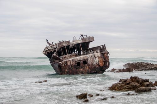 Free A rusted shipwreck on the rocky coastline of South Africa, surrounded by waves and seabirds. Stock Photo