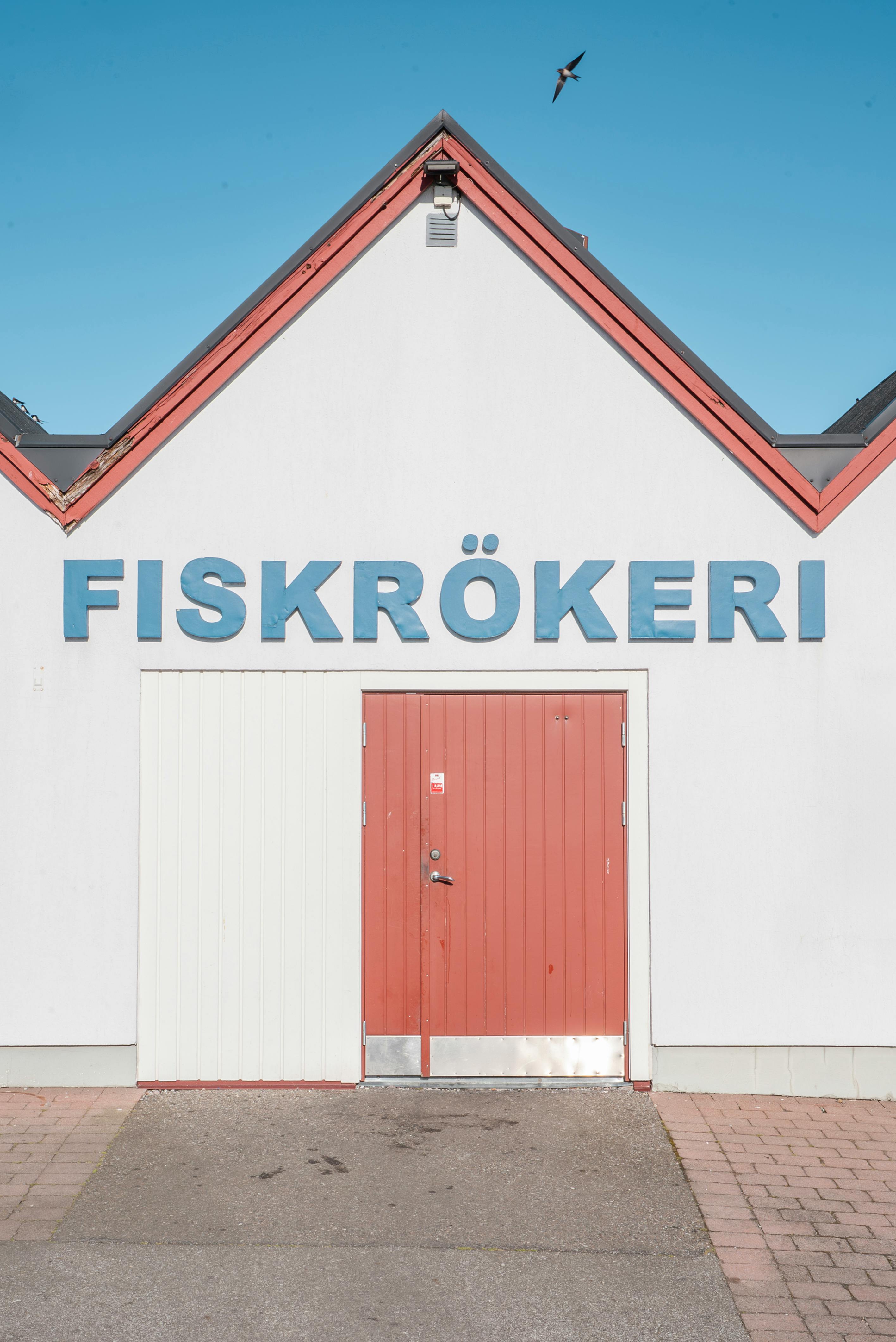Front view of a traditional Swedish fiskrökeri with red doors and blue sky in the background.