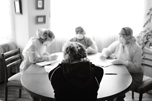 Healthcare team in protective equipment engaging with a person at a table, highlighting medical discussion in pandemic setting.