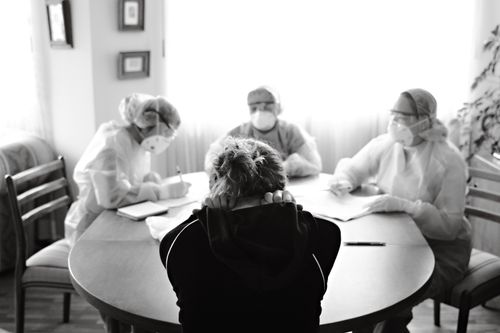 Free Healthcare team in protective equipment engaging with a person at a table, highlighting medical discussion in pandemic setting. Stock Photo