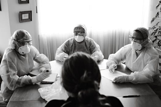 Black and white photo of healthcare team in PPE holding a meeting indoors.
