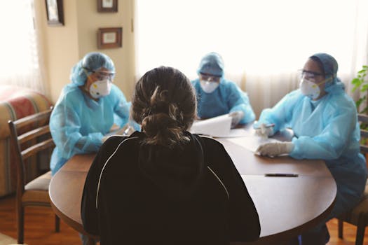 Healthcare workers in protective gear consult with a patient at home, ensuring safety and care.
