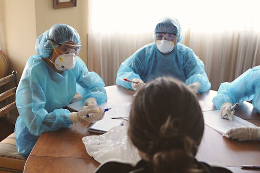 Photo by DΛVΞ GΛRCIΛ Healthcare professionals in PPE discuss operations during a meeting indoors.