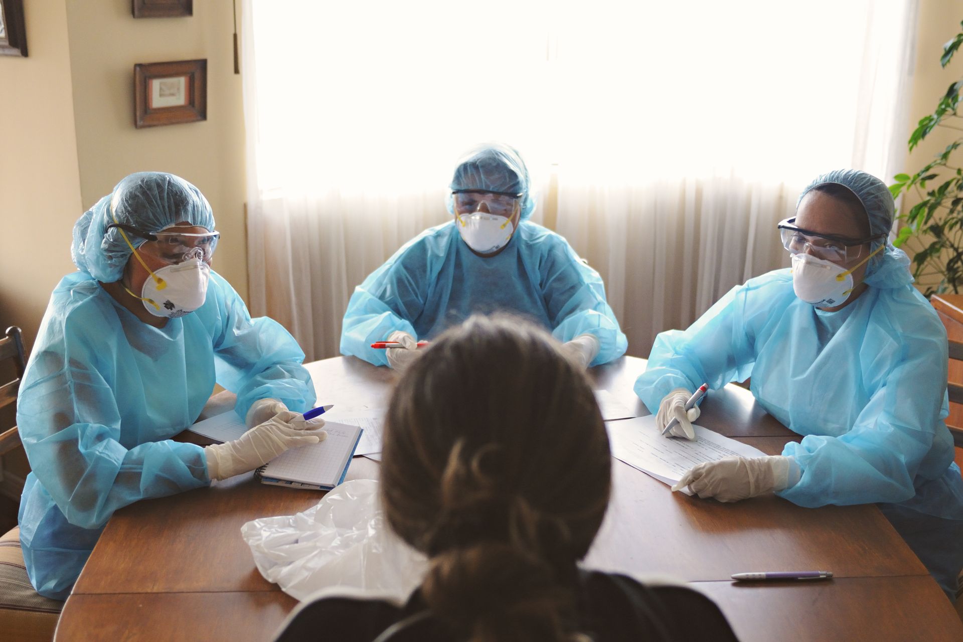 Three healthcare professionals in PPE discuss patient care indoors.
