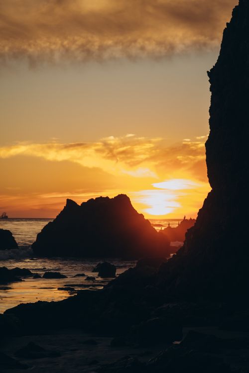 Free Dramatic sunset over Malibu Beach with silhouetted cliffs and vivid sky. Stock Photo
