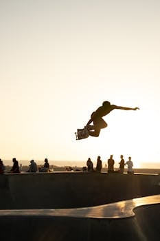 Silhouette of a skateboarder performing a trick at sunset in Venice Beach, Los Angeles.
