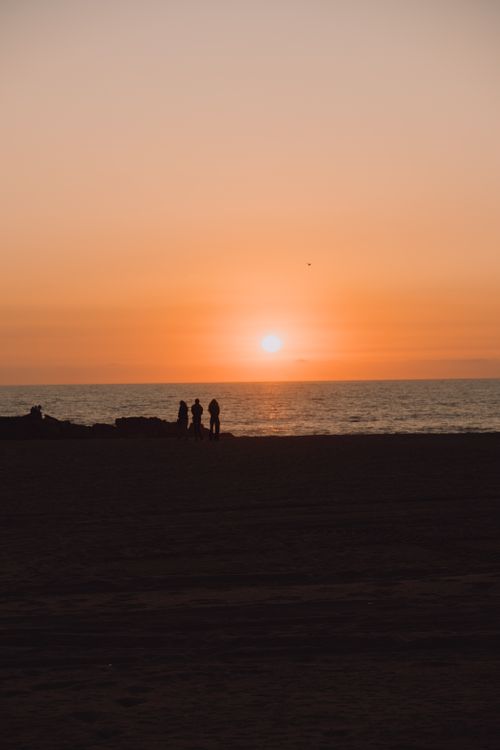 Free Silhouetted figures watch a stunning sunset over the ocean at a Los Angeles beach. Stock Photo