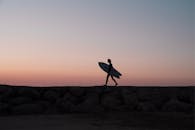 在日落之时，葡萄牙的岩石海滩上，一名冲浪者正在散步