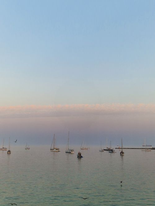 Free Serene morning view of sailboats on calm water under a pastel sunrise sky. Stock Photo