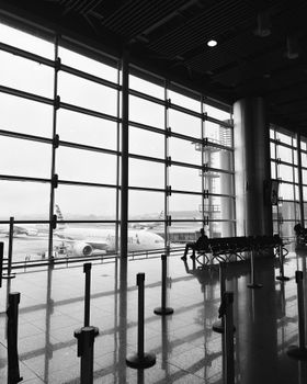 Black and white image of a modern airport terminal overlooking a parked airplane.