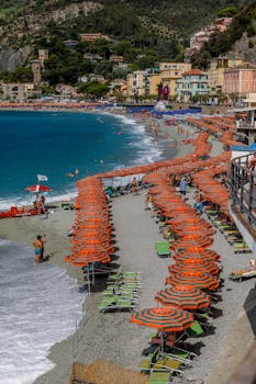 A lively beach in Monterosso with orange umbrellas, colorful buildings, and a scenic coastline.