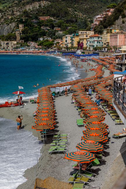 A lively beach in Monterosso with orange umbrellas, colorful buildings, and a scenic coastline.