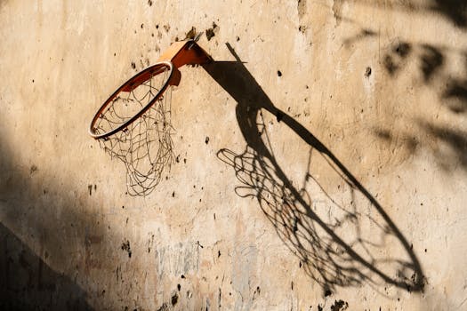 An old basketball hoop with shadow on a sunlit stone wall, creating a nostalgic urban feel.