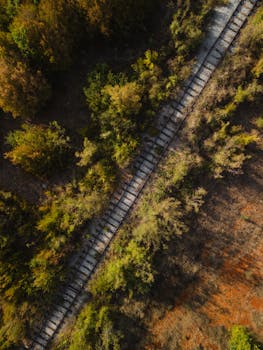 Aerial shot of a railway cutting through lush greenery in Albania during autumn.