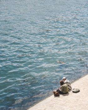 A couple sitting by the Seine River, enjoying the serene Parisian setting on a sunny day.