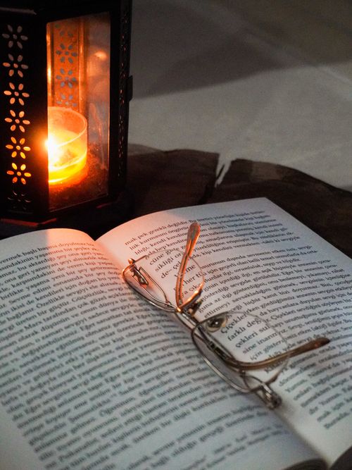 Free Warm candlelit setting with glasses on an open book, ideal for cozy reading themes. Stock Photo