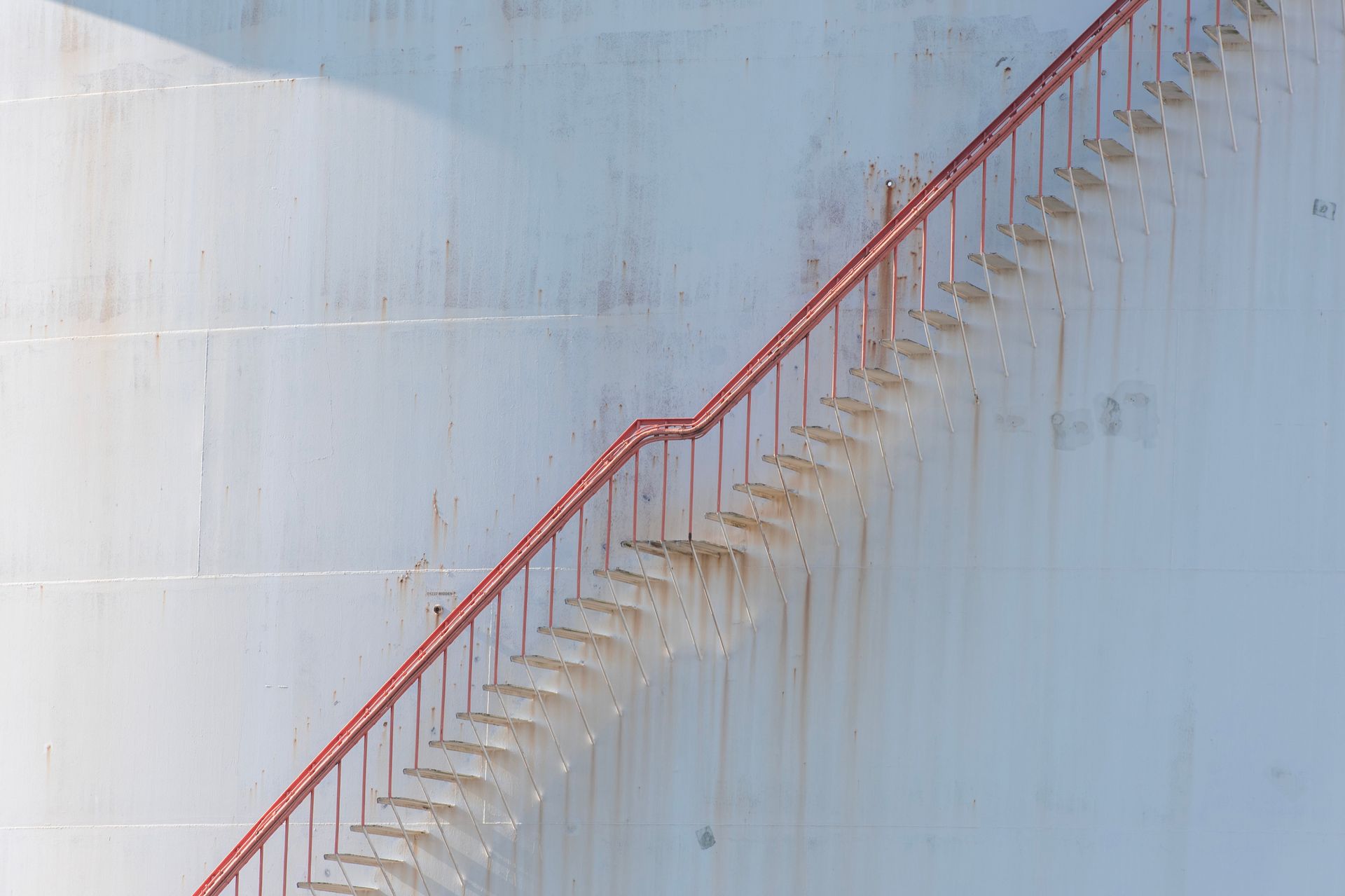 Red metal stairs on a large, weathered industrial tank with visible rust stains.