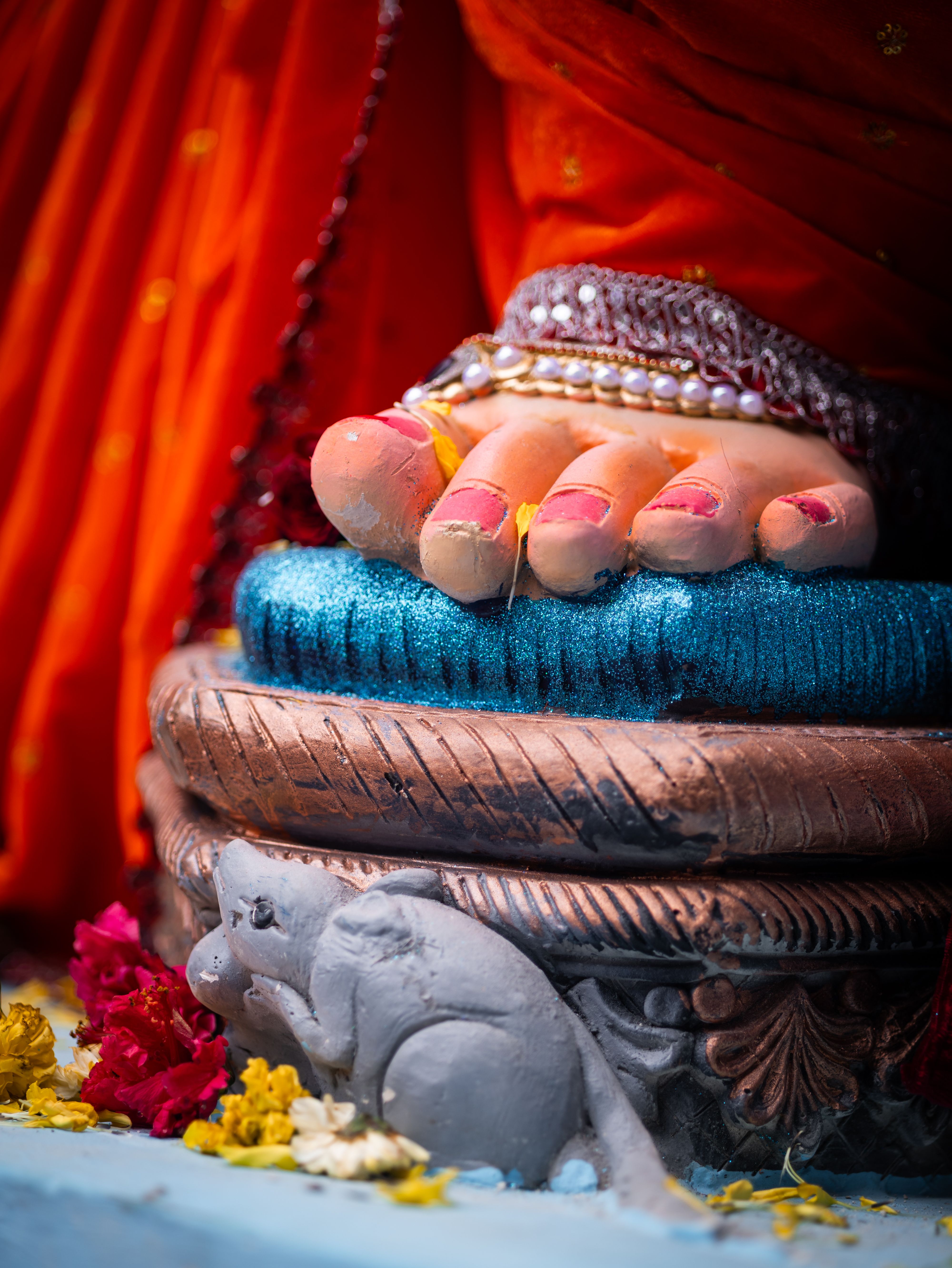 A detailed view of a Hindu statue foot with vibrant decorations and flowers.