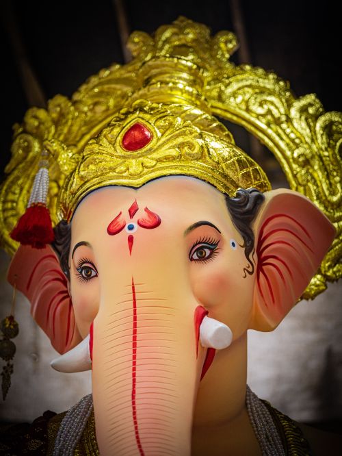 Free Close-up of a detailed Ganesh idol adorned with a gold crown, vibrant colors, and cultural decorations. Stock Photo