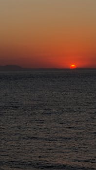 A serene sunset view over the ocean with vibrant orange and red tones.